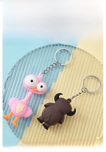 Detail of pink bird and brown bull cartoon keychains on a textured glass tray