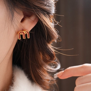 Detail showing red enamel M letter stud earring in gold-tone finish worn by model