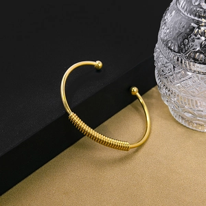 Detail of gold-plated open bangle featuring textured screw thread design and bead ends