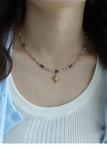 Detail of beaded star necklace with tiger eye stones on white knit sweater