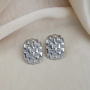Détail macro de boucles d'oreilles tissées en acier inoxydable argenté sur tissu beige
