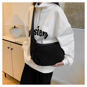 Detail of a black crescent canvas crossbody bag styled with a white branded sweatshirt