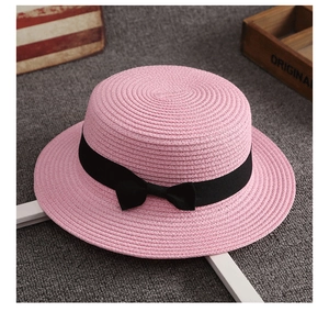 Dettaglio della trama di paglia intrecciata rosa e del fiocco nero sul cappello estivo