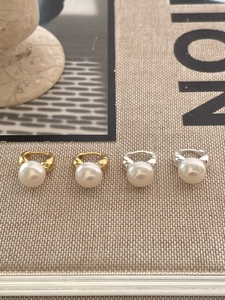 Detail of 925 sterling silver pearl earrings in gold and silver finishes on beige fabric