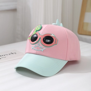 Détail de la casquette enfant rose et verte avec dinosaure 3D et lunettes de soleil
