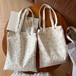 Three floral canvas tote bags in beige, pink, and purple spread on a wooden table