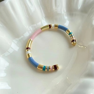 Detail of colorful enamel gold open cuff bracelet on white ceramic plate with soft light