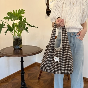 Detail of a brown plaid tote bag featuring a colorful sonaka beaute fabric label on the front