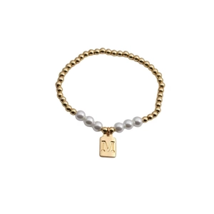 Gold beaded bracelet with five white pearls and a square letter M pendant on white background