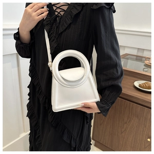 Close-up of white crossbody bag with large circular handle on model in black dress