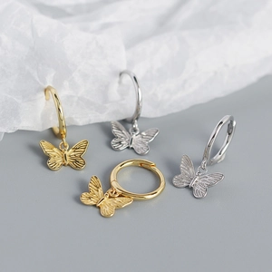 Detalle de los pendientes de aro con mariposa en oro y plata sobre papel texturizado