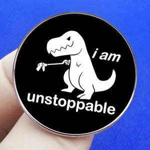Funny cartoon T-Rex pin badge with I Am Unstoppable text on black metal background