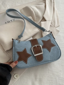 Detail of light blue denim baguette bag with star patches and large silver metal buckle