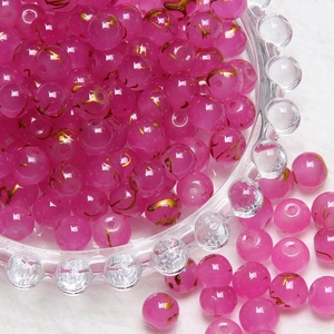 Close-up of 8mm pink frosted glass beads with gold floral patterns in a glass bowl