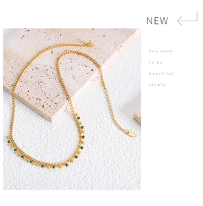Detail of gold titanium necklace with green beads and adjustable clasp on stone surface