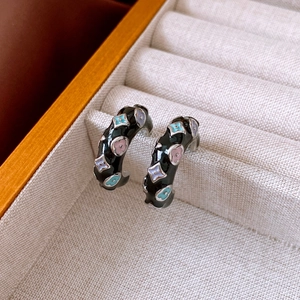 Detailed macro view of black enamel floral earrings with colorful petals on a display case