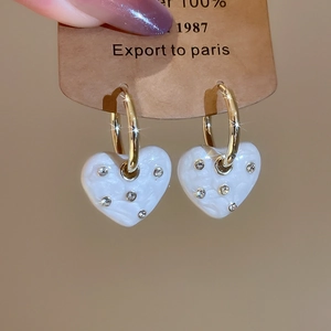 Close-up of gold heart earrings with white enamel texture and sparkling crystal accents
