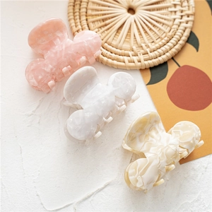 Three acetate shark hair clips in pink, pure white, and marble white on a woven mat