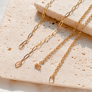 Close-up of gold-plated stainless steel paperclip and curb chains on textured stone