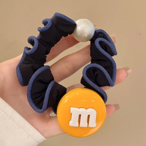 Détail d'élastique à cheveux en tissu avec perle blanche et breloque jaune lettre m