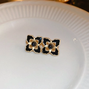 Macro detail of retro black enamel flower stud earrings with gold plating and center beads