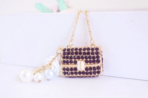 Detailed macro view of golden bag pendant with black rhinestones and white pearl accent