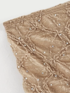 Détail de tissu en dentelle tricotée beige avec strass et motifs floraux brodés