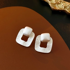 Macro shot of matte silver hollow square earrings with handcrafted texture on leather background