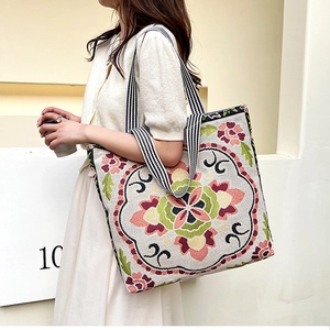 Detail of floral embroidery on a beige canvas tote bag with striped handles shown on model