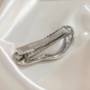 Macro detail of silver irregular hollow metal hairpin on white silk background