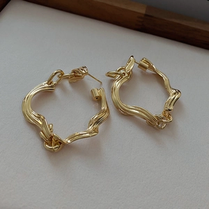 Macro shot of gold-plated twisted wave earrings with irregular textured geometric details
