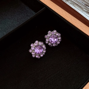 Detailed macro view of silver flower stud earrings with purple center rhinestone and crystals