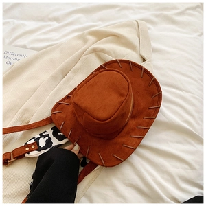 Detail of a brown suede cowboy hat bag featuring decorative stitching and cow print straps