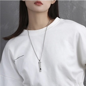 Close-up of a functional silver whistle necklace worn by a model against a grey wall