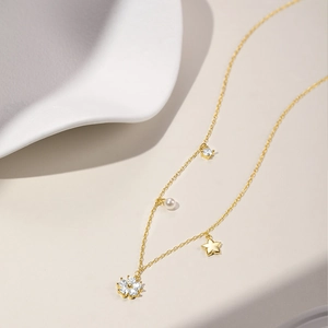 Detail of gold star and pearl necklace with sparkling zircon flower pendant on ceramic