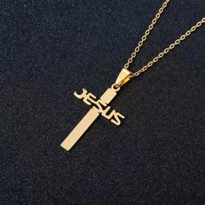 Dettaglio del ciondolo a croce in acciaio dorato con scritta JESUS su sfondo nero sabbiato