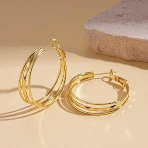 Detailed view of layered golden metallic earrings with geometric diamond textures and raw stone