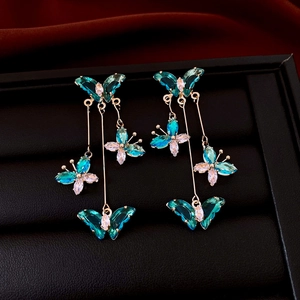 Macro shot of gold butterfly tassel earrings with blue zircon crystals on red velvet
