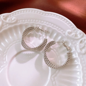 Macro shot of silver woven beaded hoop earrings on a decorative white porcelain plate