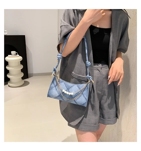 Détail du sac croissant en denim bleu avec motif matelassé, chaîne dorée et perles