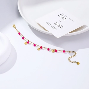 Close-up of a double-layer gold stainless steel bracelet with magenta pink beads and charms