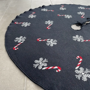 Detail of black knitted Christmas tree skirt with white snowflakes and candy cane patterns