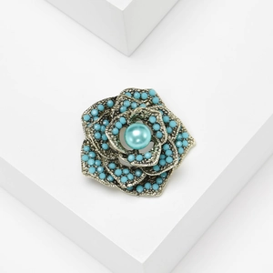 Vintage bronze flower brooch with turquoise beads and pearl on white geometric background