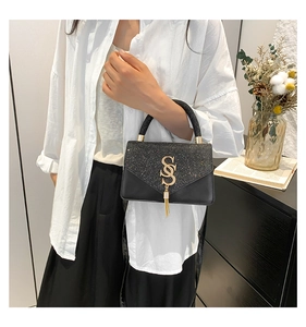 Chic black crossbody bag with gold tassel and sequin flap detail on a stylish model