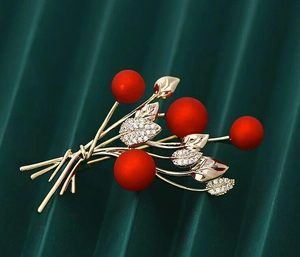 Detail of a floral brooch with dark red berries and gold leaves with sparkling crystals