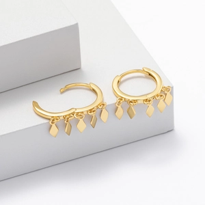 Detailed view of gold hoop earrings with rhombus pendants on a geometric background
