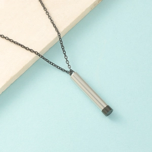 Close-up of a silver cylindrical pendant with black detail on a black chain necklace