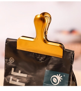 Close-up of golden brushed metal food clip sealing a coffee bag with secure grip