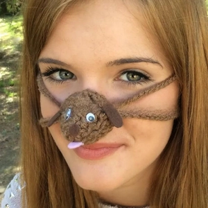 Detail of a handmade brown knit dog nose warmer with 3D ears and pink tongue