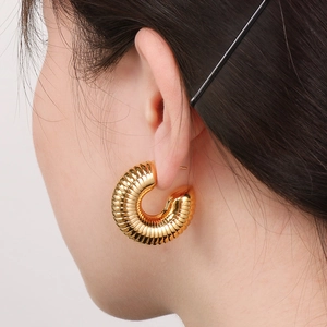 Macro view of gold-plated hollow C-shape earrings with spiral texture on the ear